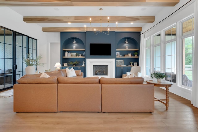 living area featuring light wood finished floors, a fireplace, beam ceiling, and built in shelves
