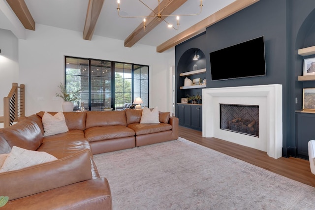living area with an inviting chandelier, wood finished floors, a fireplace, beamed ceiling, and built in shelves