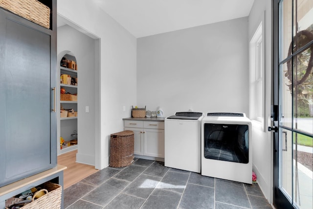 laundry area featuring stone tile flooring, arched walkways, cabinet space, and independent washer and dryer
