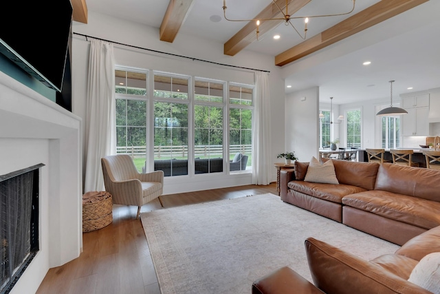living room featuring a fireplace, light wood-type flooring, beam ceiling, and a notable chandelier