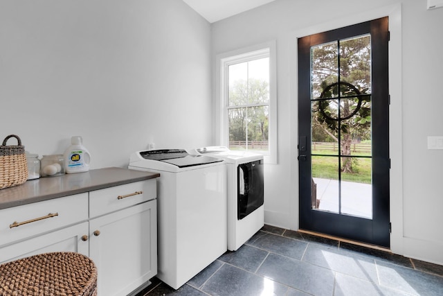 clothes washing area featuring washer and clothes dryer, cabinet space, and stone tile floors