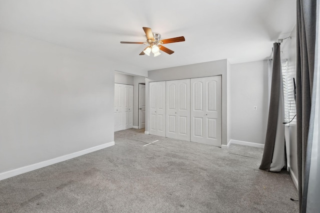 unfurnished bedroom featuring two closets, a ceiling fan, baseboards, and carpet