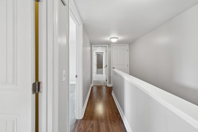hall featuring baseboards, dark wood finished floors, and an upstairs landing