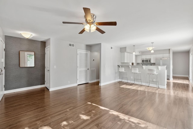 unfurnished living room featuring baseboards, visible vents, ceiling fan, and wood finished floors