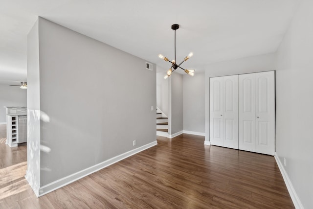 unfurnished dining area featuring baseboards, ceiling fan with notable chandelier, wood finished floors, and stairway