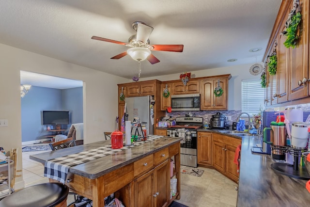 kitchen with dark countertops, ceiling fan, a sink, brown cabinetry, and stainless steel appliances