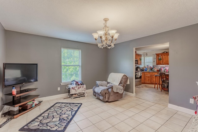 living area featuring light tile patterned floors, baseboards, a textured ceiling, and a notable chandelier