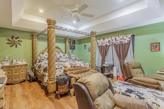 bedroom with light wood-style flooring, a raised ceiling, and ceiling fan