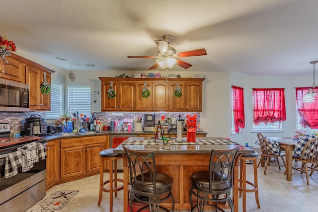 kitchen with appliances with stainless steel finishes, a ceiling fan, and brown cabinets