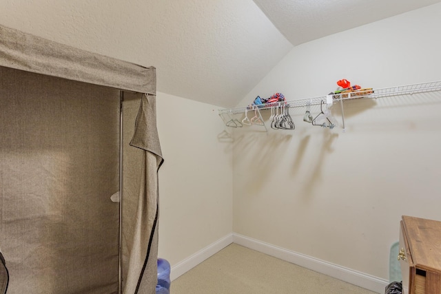 walk in closet with vaulted ceiling and light colored carpet