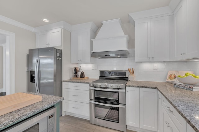 kitchen with appliances with stainless steel finishes, white cabinets, decorative backsplash, and custom range hood