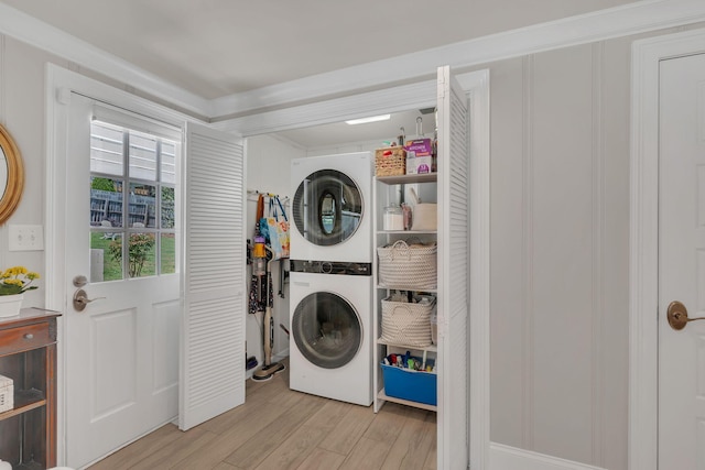 laundry room featuring stacked washer / drying machine, ornamental molding, laundry area, and light wood-style floors