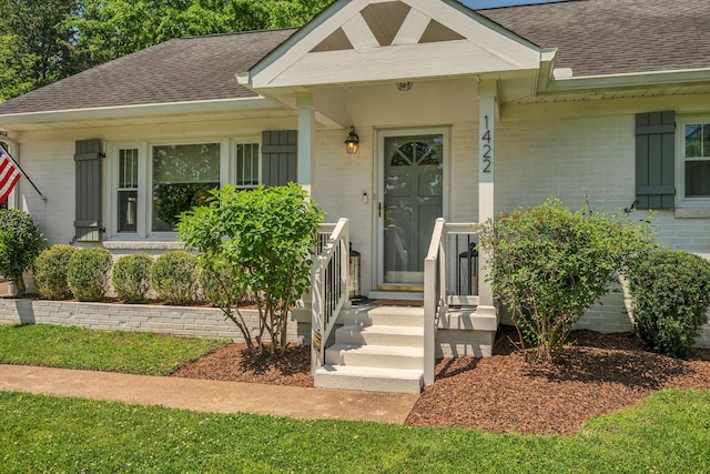 entrance to property with roof with shingles and brick siding