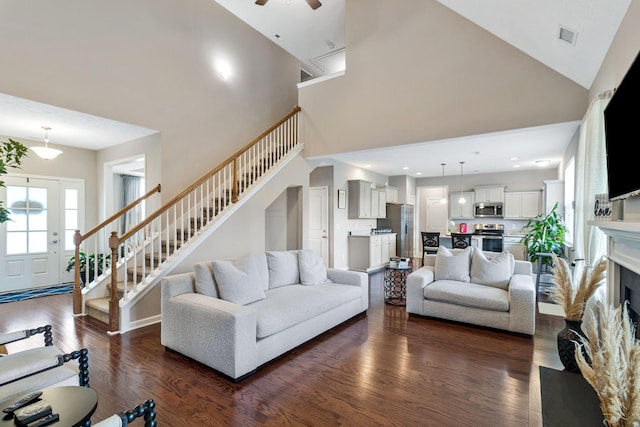 living room featuring dark wood-type flooring, a ceiling fan, a towering ceiling, and stairway