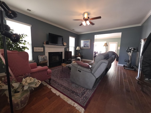 living area with crown molding, ceiling fan, a fireplace, wood-type flooring, and visible vents