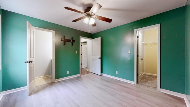 unfurnished bedroom with a ceiling fan, light wood-type flooring, baseboards, a closet, and a spacious closet
