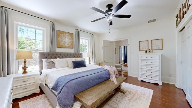 bedroom with a ceiling fan, visible vents, crown molding, dark wood finished floors, and a closet