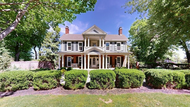 greek revival house featuring a porch, fence, and a chimney