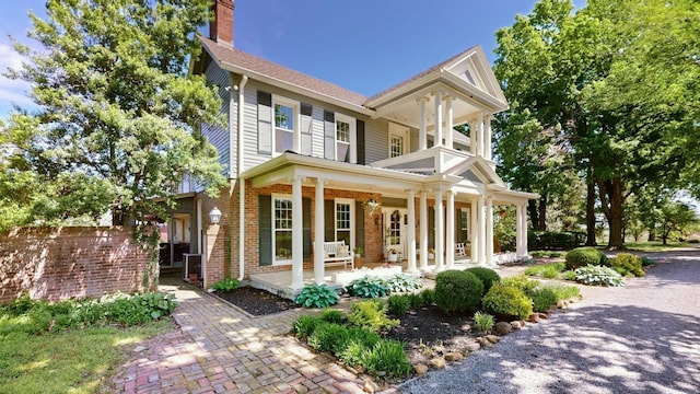 back of house with covered porch, brick siding, and a chimney