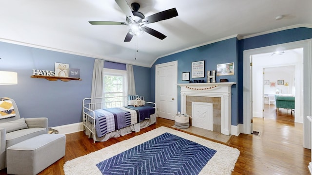 bedroom with ornamental molding, wood finished floors, and a tile fireplace
