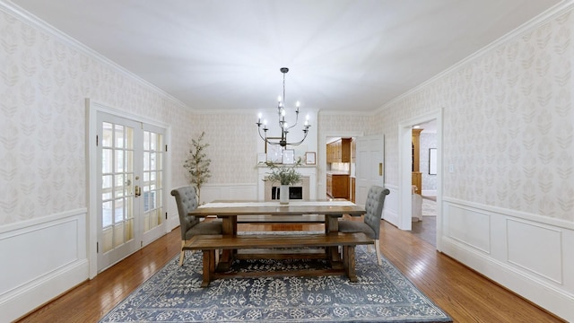 dining space featuring an inviting chandelier, crown molding, wood finished floors, wallpapered walls, and a wainscoted wall