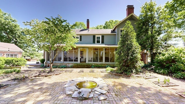 rear view of house with a sunroom, a patio area, and a chimney