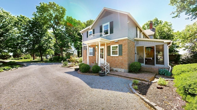 view of front of house with a balcony, a chimney, driveway, and brick siding