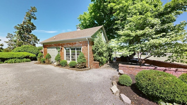 view of side of property featuring a chimney, brick siding, an outdoor structure, a patio, and a shingled roof