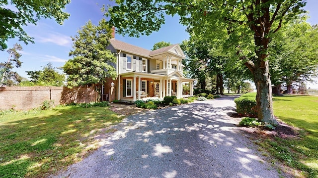 view of front of property featuring covered porch, a chimney, brick siding, fence, and a front lawn