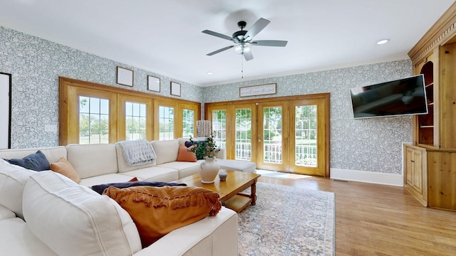 living area featuring light wood-type flooring, ceiling fan, a healthy amount of sunlight, and wallpapered walls