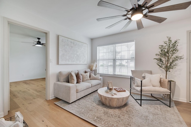 living area featuring light wood-style floors, a ceiling fan, and baseboards
