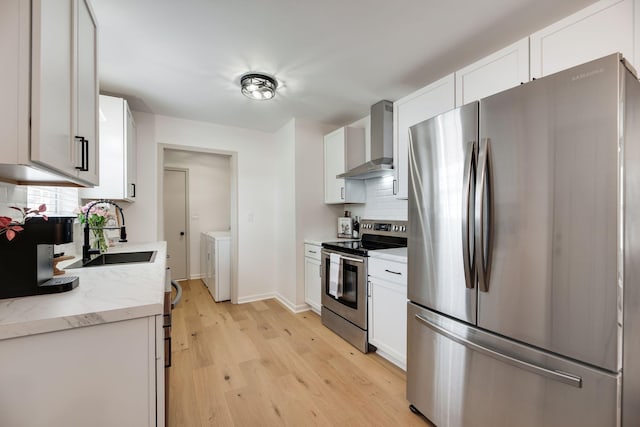 kitchen featuring wall chimney range hood, backsplash, appliances with stainless steel finishes, a sink, and washer and clothes dryer