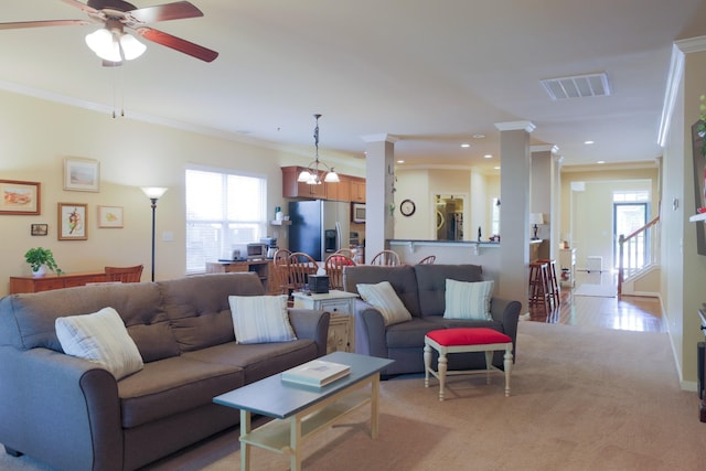 living room with plenty of natural light, ornamental molding, ceiling fan with notable chandelier, and visible vents