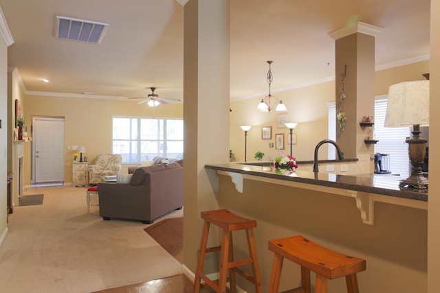 kitchen featuring crown molding, a breakfast bar area, a ceiling fan, and visible vents