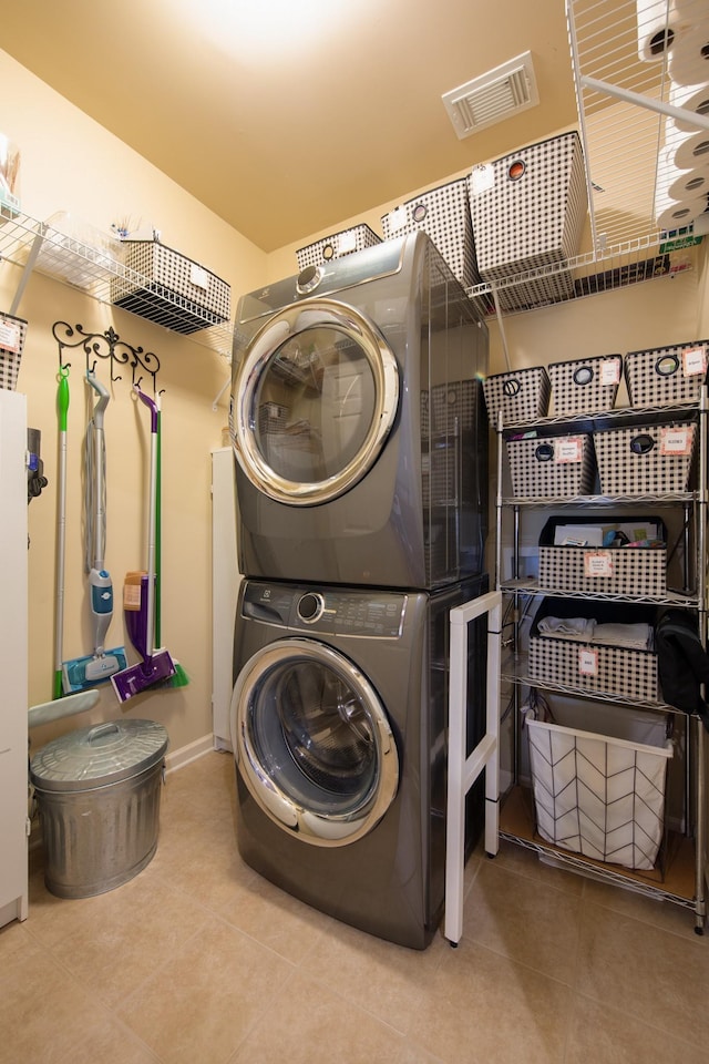 clothes washing area featuring stacked washer and dryer, laundry area, visible vents, and tile patterned flooring