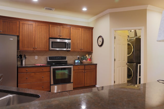 kitchen featuring visible vents, stacked washer and clothes dryer, ornamental molding, tasteful backsplash, and stainless steel appliances