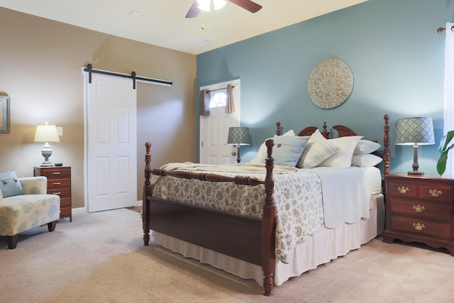 bedroom with a ceiling fan, a barn door, and light colored carpet