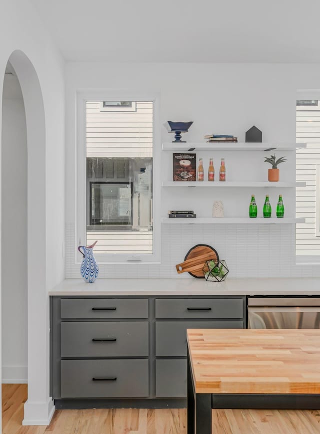 bar with arched walkways, baseboards, stainless steel dishwasher, and light wood-style flooring
