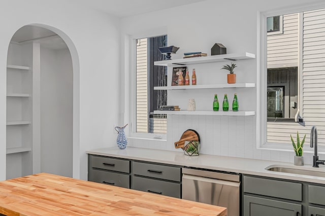 bar featuring stainless steel dishwasher, arched walkways, built in shelves, and a sink