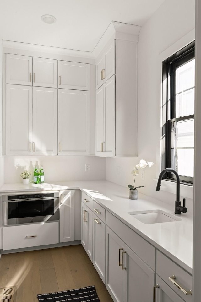 kitchen featuring visible vents, wood finished floors, a sink, light countertops, and white cabinets