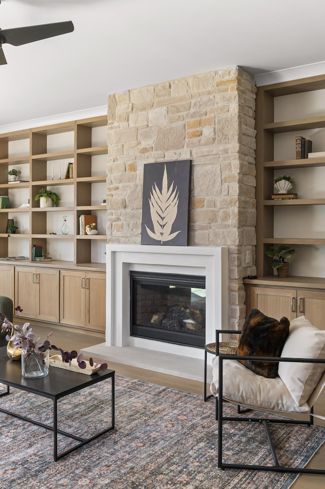 living room with a ceiling fan, built in features, a glass covered fireplace, and wood finished floors