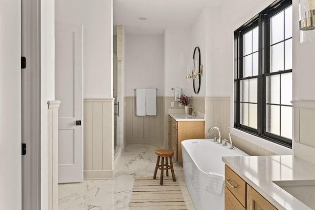 bathroom with marble finish floor, a wainscoted wall, two vanities, a sink, and a stall shower