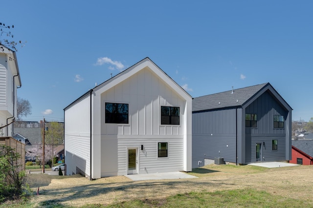 rear view of house with board and batten siding, a patio, a lawn, and central air condition unit