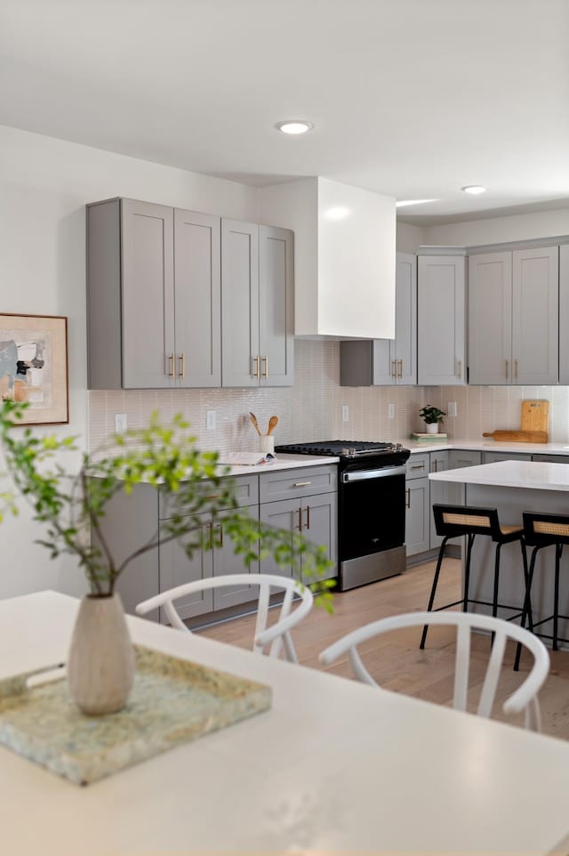 kitchen with stainless steel range with gas cooktop, gray cabinets, light wood finished floors, and tasteful backsplash