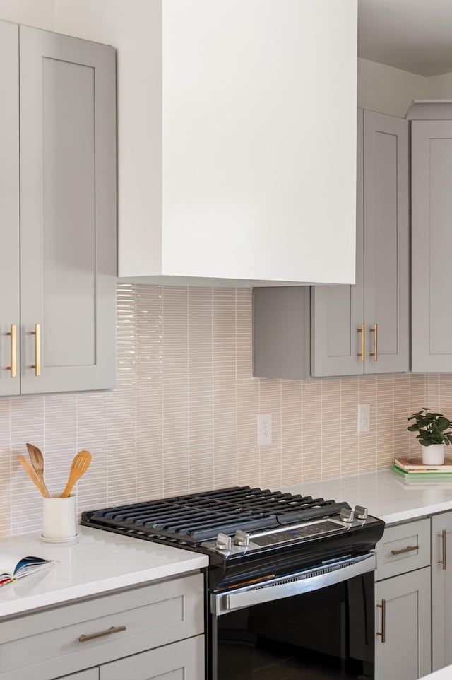 kitchen featuring light countertops, decorative backsplash, gray cabinetry, and stainless steel range with gas cooktop