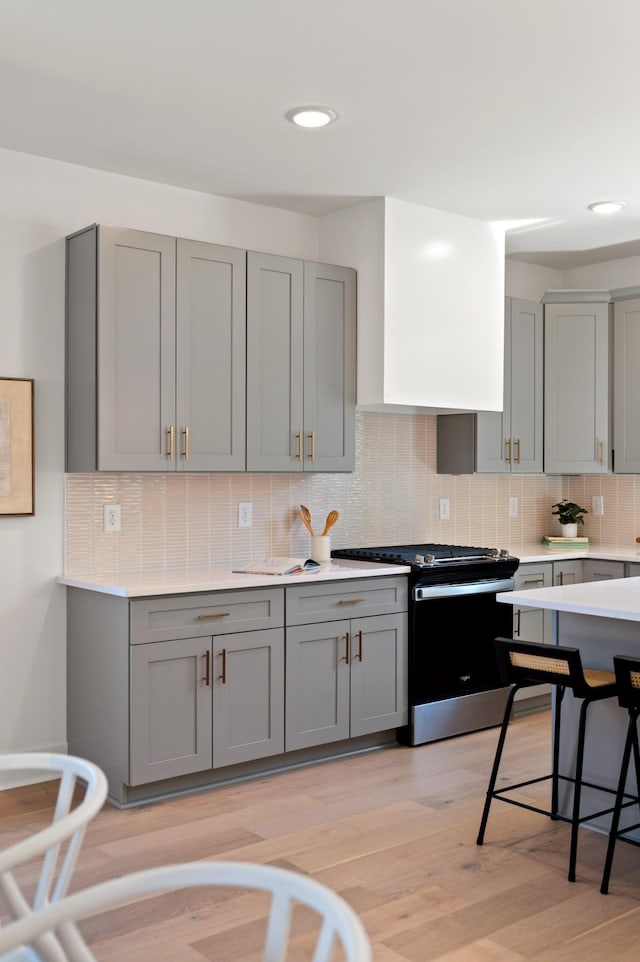 kitchen with light countertops, decorative backsplash, gas stove, and gray cabinetry