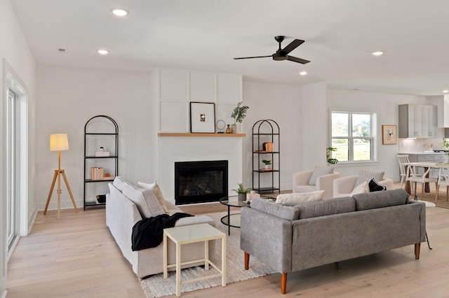 living area featuring recessed lighting, light wood-style flooring, ceiling fan, and a glass covered fireplace