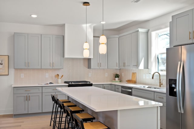 kitchen featuring a kitchen bar, light countertops, a sink, appliances with stainless steel finishes, and gray cabinetry
