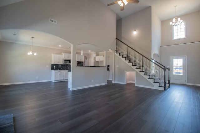 unfurnished living room featuring plenty of natural light, ceiling fan with notable chandelier, a towering ceiling, dark wood-style floors, and stairway