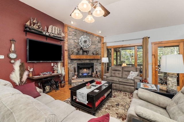living room with a stone fireplace, vaulted ceiling, wood finished floors, and a chandelier